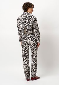 Geprinte broeken en bijpassende jas gemaakt van textuurstof. Bevat een golvend zwart en crèmekleurig ontwerp. Inclusief een uitsnijding op de rug.