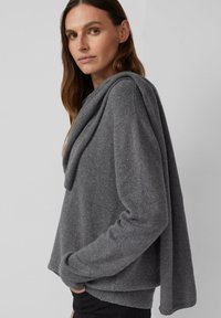 Grauer Pullover mit einem drapierten Ausschnitt, langen Ärmeln und geripptem Saum. Hergestellt aus gestricktem Stoff mit weicher Textur.