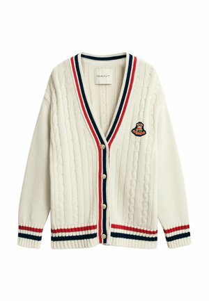 Crème kabelgebreide cardigan met rood, marineblauw en witte gestreepte bies, knopen aan de voorkant en geborduurd wapenschild op de borst.