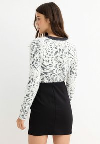 Jersey de punto blanco y negro con patrón, de manga larga y cuello de canalé, combinado con una falda negra ajustada. Textura suave y esponjosa.