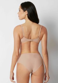 Nude bh med justerbara band och hysstycke, i kombination med matchande högmidjade trosor, slät textur, minimalistisk design.
