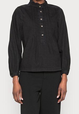 Czarna bluzka z długim rękawem, z marszczonym wysokim kołnierzem, pionowymi zakładkami i pięcioma guziczkami z przodu, noszona z czarnymi spodniami.