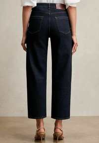 Mörkblå denim byxor med vida ben, sydd midjeresår, två bakfickor och en läderlapp med texten "REISS." Har en ren finish.