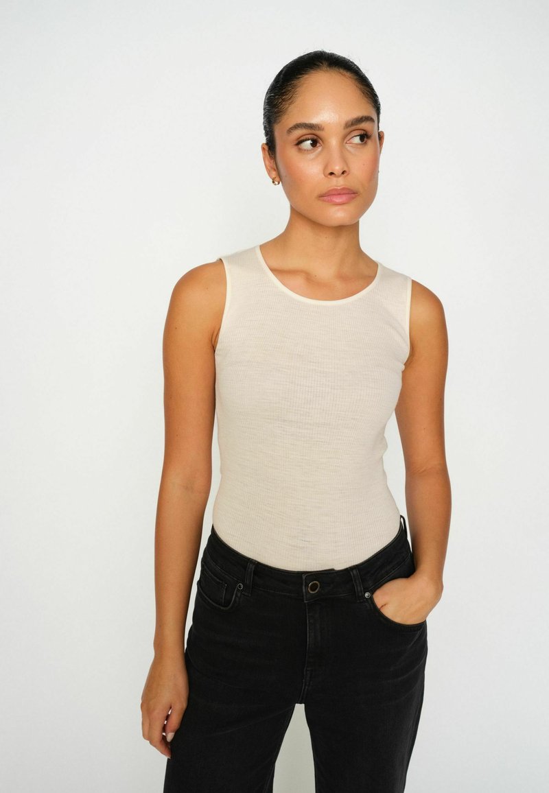 Beige ribbed tank top with a round neckline and sleeveless design, paired with black high-waisted pants. Flat texture and fitted silhouette.