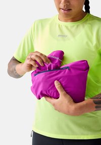 Roze ritssluiter tas wordt vastgehouden, gemaakt van glad stof. Een persoon draagt een felgele, gestructureerde T-shirt met korte mouwen.