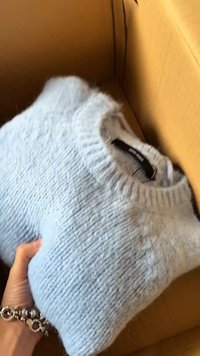 Main tenant un pull en tricot bleu clair plié à l'intérieur d'une boîte en carton marron.