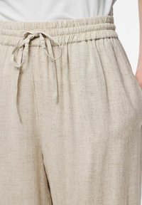 Pantalons en mélange de lin beige clair avec une taille élastique et un cordon de serrage. Comprend des poches latérales et une finition en tissu texturé.