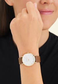 Bruine leren bandhorloge met een witte wijzerplaat, gouden uurmarkers en een gouden bezel. Minimalistisch design met een klassieke uitstraling.