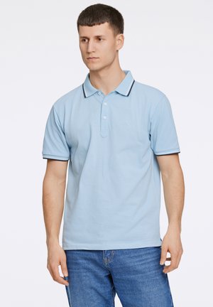 Polo en coton bleu clair avec une patte de boutonnage à deux boutons, un col rayé bleu marine et blanc, et des manches courtes. Porté avec un jean bleu.