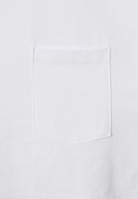 Bílý bavlněný tričko s jednou pečlivě našitou kapsou. Hladký povrch s minimalistickým designem, bez dalších vzorů nebo grafik.