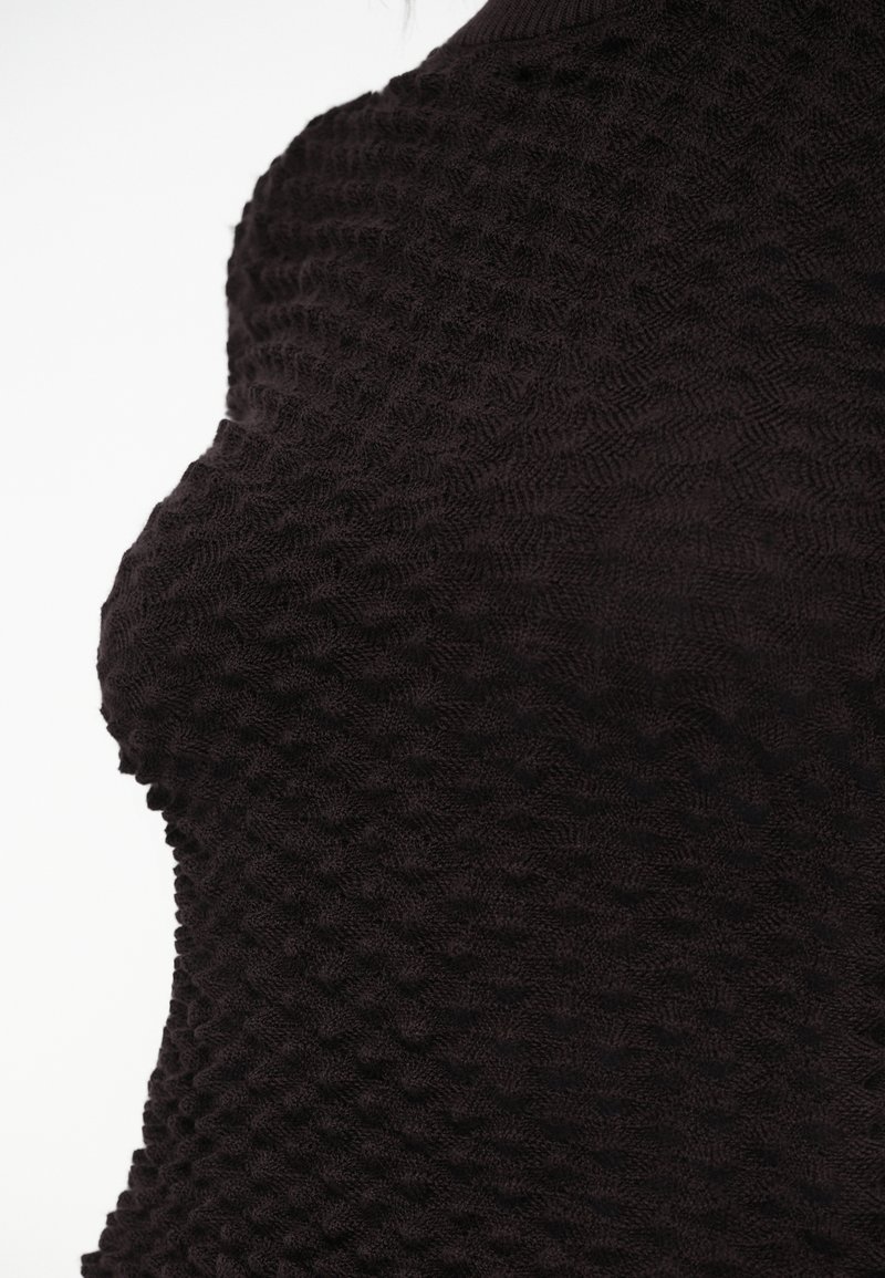 Gestructureerd zwart gebreid top met een golvend patroon, aansluitende pasvorm en ronde halslijn, die een zachte, gelaagde stofstructuur toont.