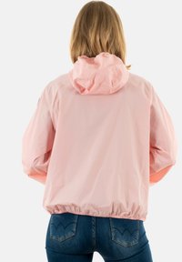 Giacca leggera rosa con cappuccio, polsini e orlo elasticizzati. Tessuto liscio con design semplice, vista da dietro. Jeans visibili.