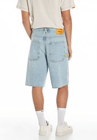 Pantalones cortos de mezclilla azul claro con un ajuste relajado, que cuentan con dos bolsillos traseros, una etiqueta naranja en la cinturilla y costuras en contraste.