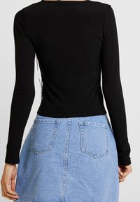 Svart ribbad långärmad topp som är kombinerad med en ljusblå denimkjol med två bakfickor och en dragkedja i mitten.