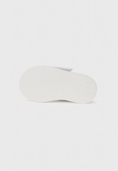 Semelle de sneaker en caoutchouc blanc avec un motif texturé en zigzags et un bout arrondi. Tige en tissu gris clair au design minimaliste et avec peu de détails de couture.