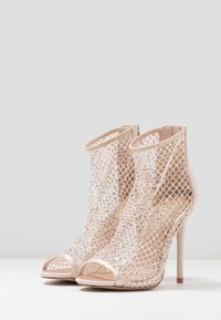 Sandalias de tacón alto con la parte delantera descubierta, base de charol nude y una superposición de malla brillante. Presentan un alto tacón de aguja y detalles intrincados.