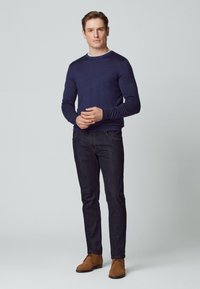 Marineblaues Langarm-Sweatshirt mit kontrastierendem Kragen, kombiniert mit dunklen Denim-Jeans und braunen Wildlederschuhen im Desert-Stil. Schlichtes, enges Design.