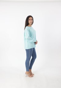 Maglione oversize verde menta chiaro con scollatura ampia e texture morbida, abbinato a jeans skinny blu e sandali trasparenti con tacco a blocco.