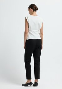 Top bianco senza maniche con design aderente e cucitura sul retro, abbinato a pantaloni neri su misura e scarpe nere con tacco basso.