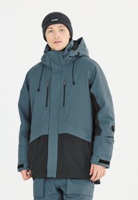 Wasserfeste Jacke in Blau-Grau mit schwarzen Akzenten, ausgestattet mit einem hohen Kragen, verstellbarem Kapuze, Reißverschlusstaschen und Klettverschluss-Manschetten.