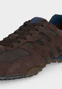 Baskets décontractées marron et noires avec des panneaux en daim et mesh, lacets noirs, doublure intérieure bleue et semelle en caoutchouc texturée.