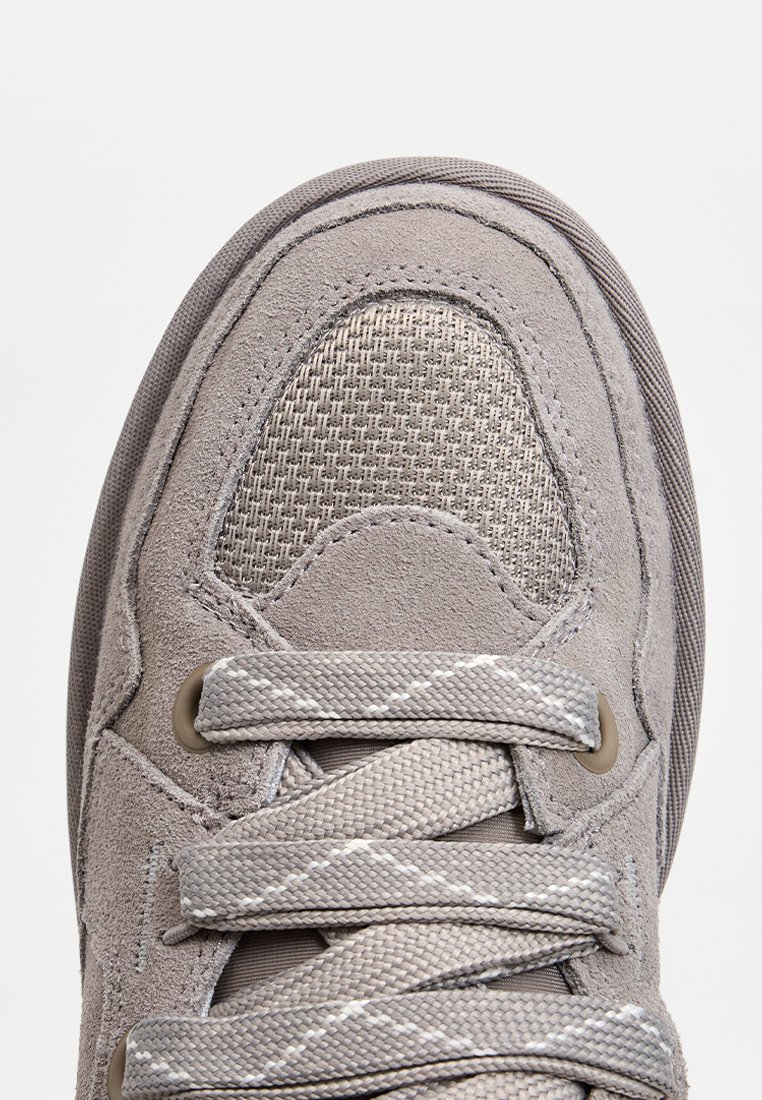Grijze sneaker met een combinatie van suède en mesh materialen, ronde neus, platte veters met grijze accenten en een gestructureerd ontwerp.