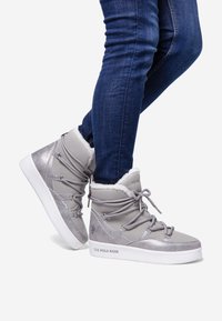 Grey high-top sneakers with suede and metallic accents, featuring faux fur trim and elastic laces. White rubber sole with branding.