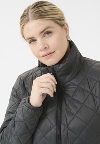 Quilted gray jacket with a high collar, zip closure, and ribbed cuffs. Features diamond-shaped stitching and glossy texture.