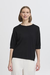 Top corto oversize nero con colletto rotondo, realizzato in tessuto morbido, abbinato a pantaloni bianchi a strisce sottili. Design semplice e moderno.