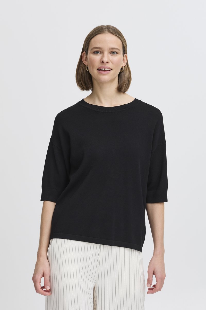 Top corto oversize nero con colletto rotondo, realizzato in tessuto morbido, abbinato a pantaloni bianchi a strisce sottili. Design semplice e moderno.