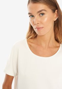 Hvid kortærmet top med en bred rund udskæring, glat tekstur og afslappet pasform, parret med et delikat ørekappe-accessory.