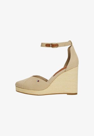 Chaussure compensée en toile beige avec une bride à la cheville, un talon en jute texturé et un petit logo sur le bout. Le design présente une pointe arrondie et un côté ouvert.