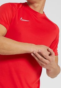 Camiseta deportiva de manga corta roja de Nike con cuello redondo y detalle del logo blanco en el pecho. Tela suave, diseño ajustado y hombros sin costuras.
