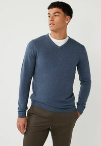 Navyblauer V-Ausschnitt-Pullover aus weichem, strukturiertem Strick. Mit langen Ärmeln und geripptem Saum. getragen über einem weißen Rundhalsausschnitt-Shirt.
