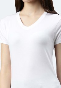 T-shirt bianco in cotone con scollo a V e maniche corte, design aderente, texture liscia e cuciture sottili lungo il collo.