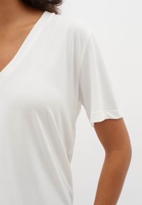 Vit kortärmad V-ringad t-shirt gjord av mjukt tyg, med en avslappnad passform och rullade ärmslut för en avslappnad stil.