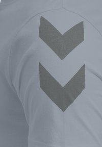 Lysegråt stof med to mørkegrå chevron-striber, der peger nedad på en buet overflade, sandsynligvis et ærme eller skulderområde.