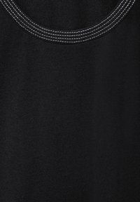 Svart tyg med en slät textur och rundad halsringning. Har kontrasterande vita sömmar längs kragen.