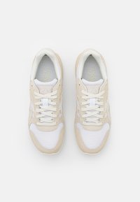 Beige and white athletic shoes with mesh and suede materials, featuring a lace-up design and logo on the tongue. Rounded toe shape.