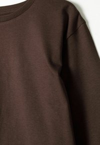Maglietta a maniche lunghe di colore marrone scuro con cucitura della spalla a vista e colletto a costine su sfondo bianco.
