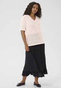 Light pink knitted v-neck top with short sleeves featuring a diamond pattern, paired with a long black skirt with ruffled hem. Black flats.