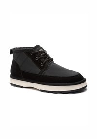 Zapato casual negro de media caña con cordones, suela blanca, paneles de ante y tela, y cuello acolchado para uso exterior.