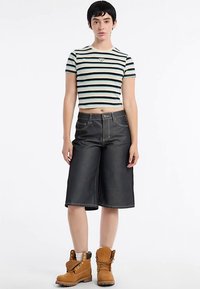 Gestreept cropped T-shirt in roomwit, donkergroen en blauw gecombineerd met donkeren denim culottes. Kenmerken contrasterende stiksels en bruine laarzen.