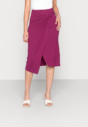 Gonna viola a lunghezza ginocchio in tessuto morbido con dettaglio anteriore annodato e design drappeggiato, abbinata a scarpe aperte sulla punta di colore chiaro.