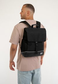 Fekete hátizsák, hajtóval, állítható pántokkal és felső fogantyúval. Elöl csattal, szürke díszítéssel és tároló zsebekkel rendelkezik.