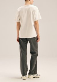 Biały bawełniany t-shirt z krótkimi rękawami, zestawiony z szarymi dżinsami o szerokich nogawkach, noszony z wielokolorowymi butami sportowymi. Prosty, casualowy design.