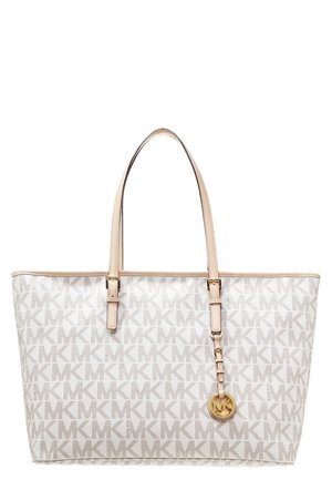 Biała torba typu tote z beżowymi rączkami, wzorem "MK" na całej powierzchni oraz złotym okrągłym breloczkiem z logo "MK" zawieszonym po prawej stronie.