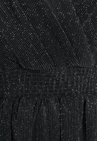 Tessuto plissettato nero con dettagli metallici argento, dotato di una cintura smock e superficie testurizzata in tutto.