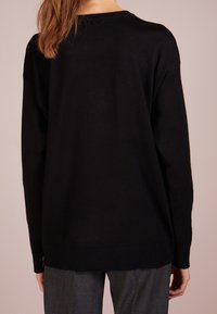 Černý pletený svetr s volnějším střihem, žebrovanými manžetami a lemem, s kulatým výstřihem a jemným bočním rozparkem. Jemná textura.