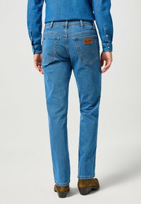 Vaqueros de mezclilla azul con un diseño de pierna recta, bolsillos traseros con un patrón de costura y una etiqueta de marca de cuero en la cinturilla.
